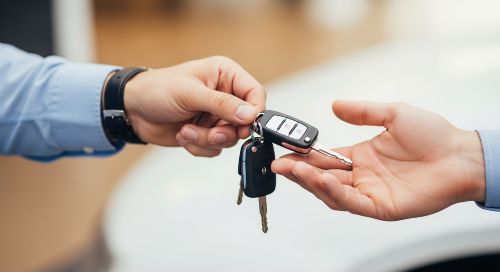 One person handing car keys to another, symbolizing borrowing a car.