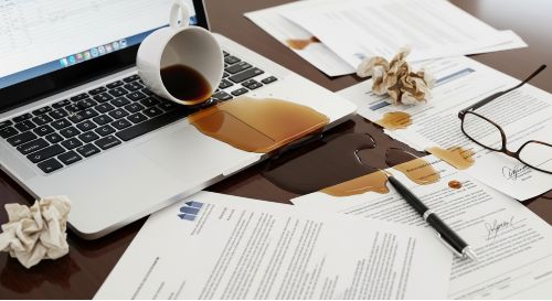 A cup of coffee spilled on an office laptop, illustrating the need for general liability insurance.