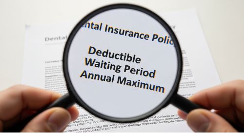 A person using a magnifying glass to read key terms like "deductible" and "waiting period" on a dental insurance policy.